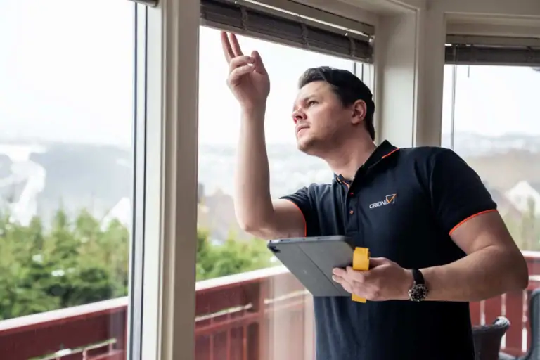 Rørlegger inspiserer vindusløsning med tablet og verktøy på veranda.