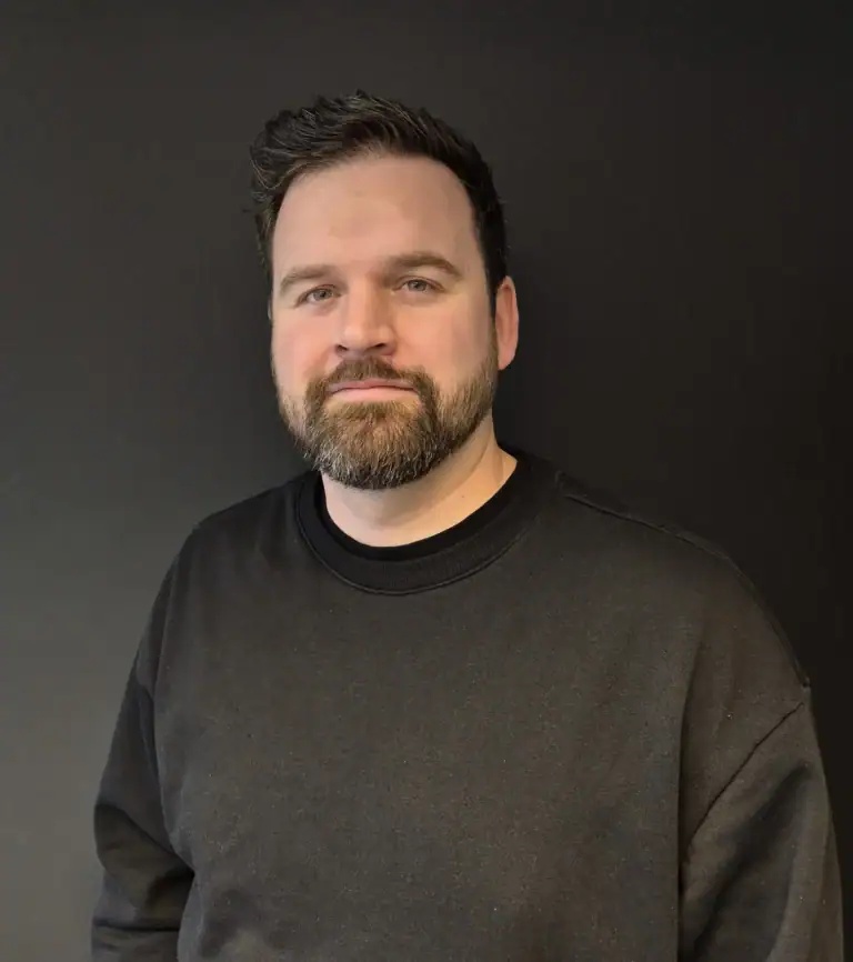 Moderne mann med skjegg i svart genser foran svart bakgrunn.